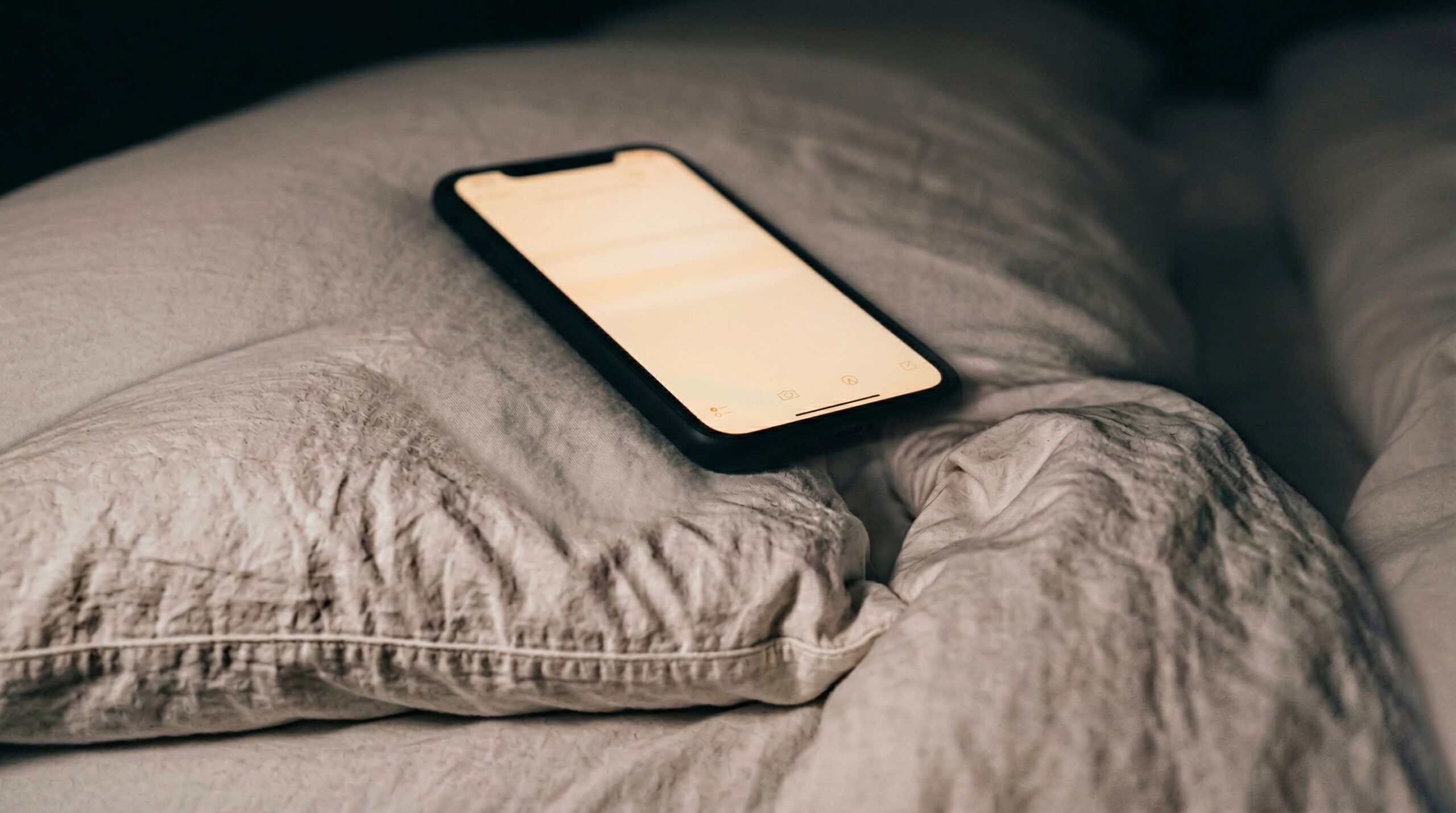 夜の寝室で枕元に置いたスマホのメモ画面が光っている様子